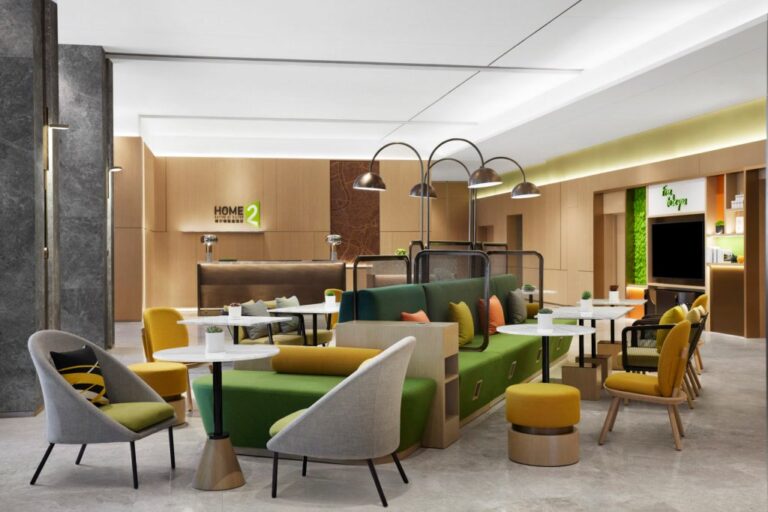 Lobby at with large seating area featuring green and yellow accents, overhead lights, tables and chairs and reception desk in Home2 Suites by Hilton Shenzhen Bao'an