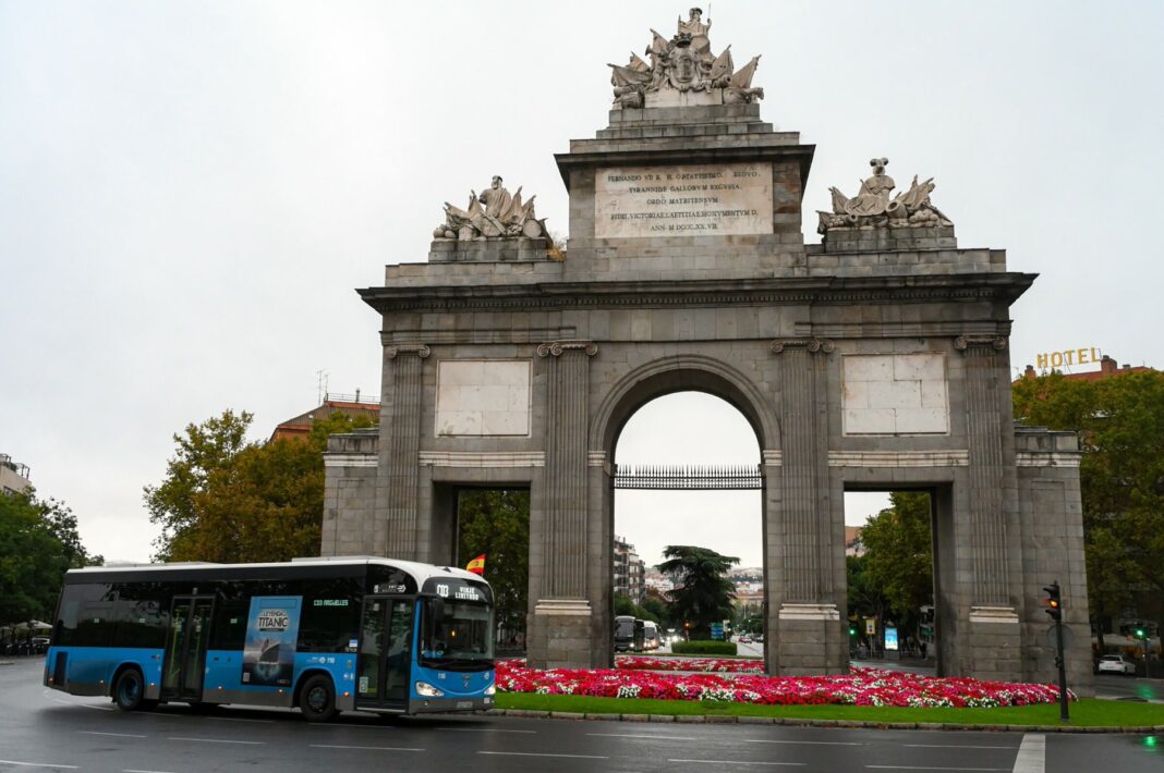 Uno de los autobuses de la EMT pasando por la Puerta de Alcalá en el Día de la Hispanidad