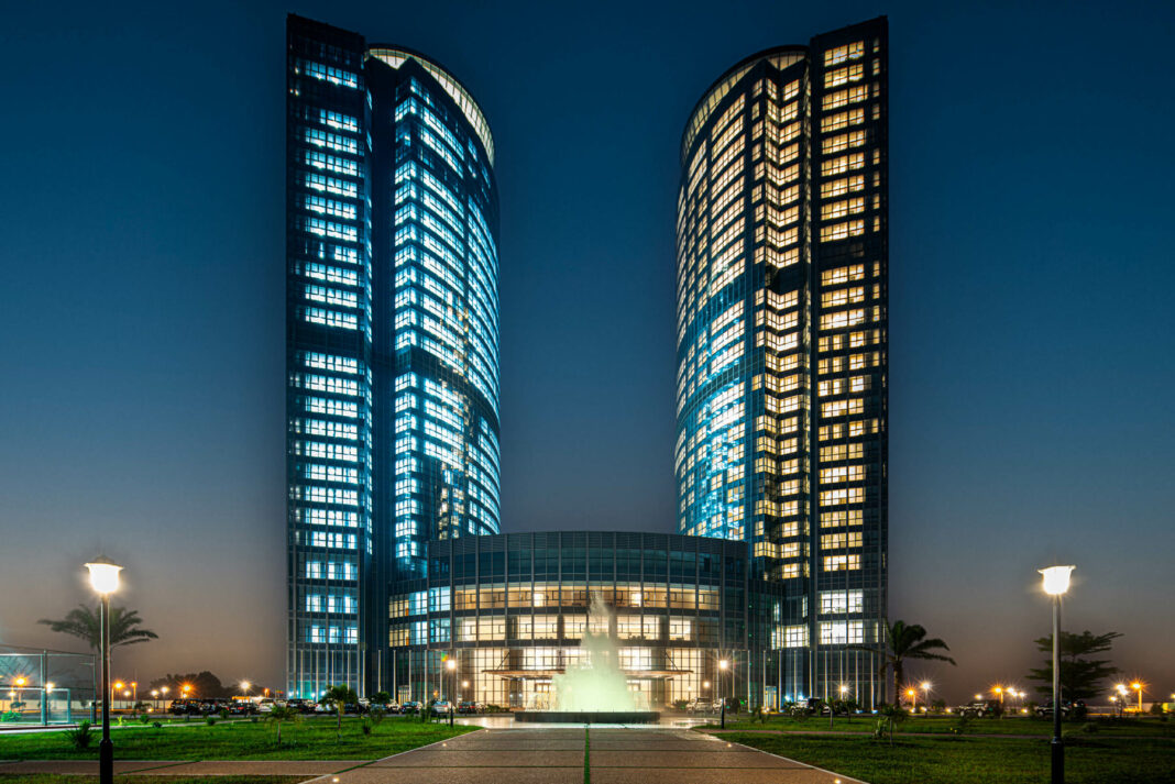 Hilton Brazzaville Les Tours Jumelles Hotel & Residences, Exterior, water fountain, sunset, palm trees, walkway, grass, parking lot, light posts